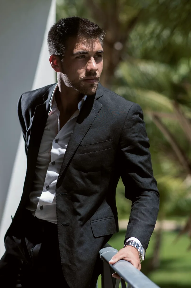 Paul in a black blazer and white shirt, leaning on a railing outdoors