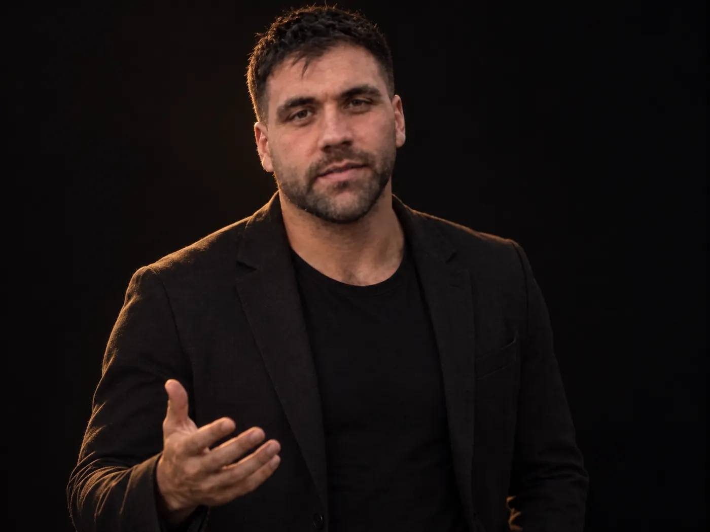 Paul in a dark blazer explaining a point with an open hand, in an empty studio